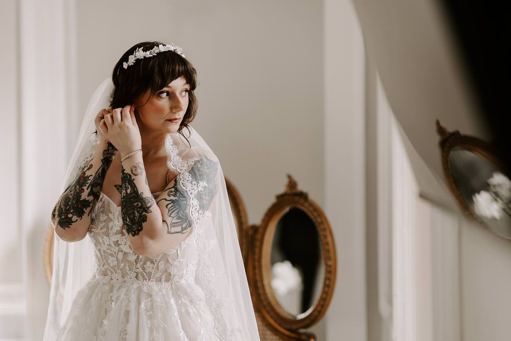 Bride in an elegant lace wedding dress getting ready in a room with mirrors.