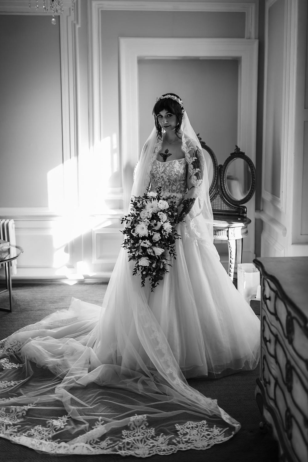 Elegant black and white bridal portrait featuring a flowing lace veil and cascading bouquet in a classic interior setting.