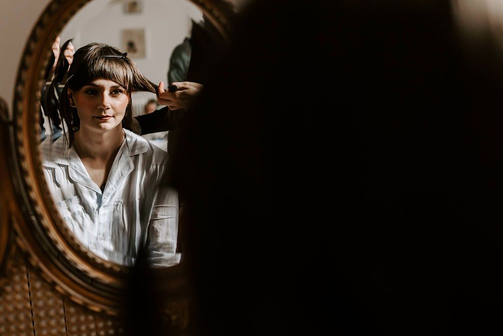 A person in a white shirt poses in front of a rustic wooden wall with moody lighting and a vintage mirror.