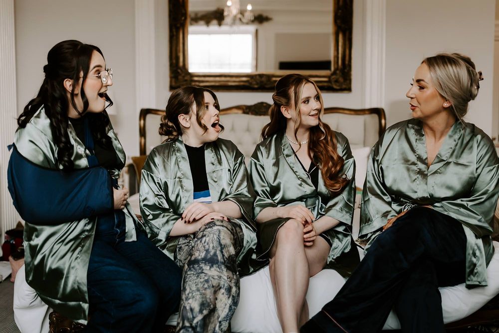 A group of bridesmaids in sage green robes share joyful moments while getting ready for a wedding.