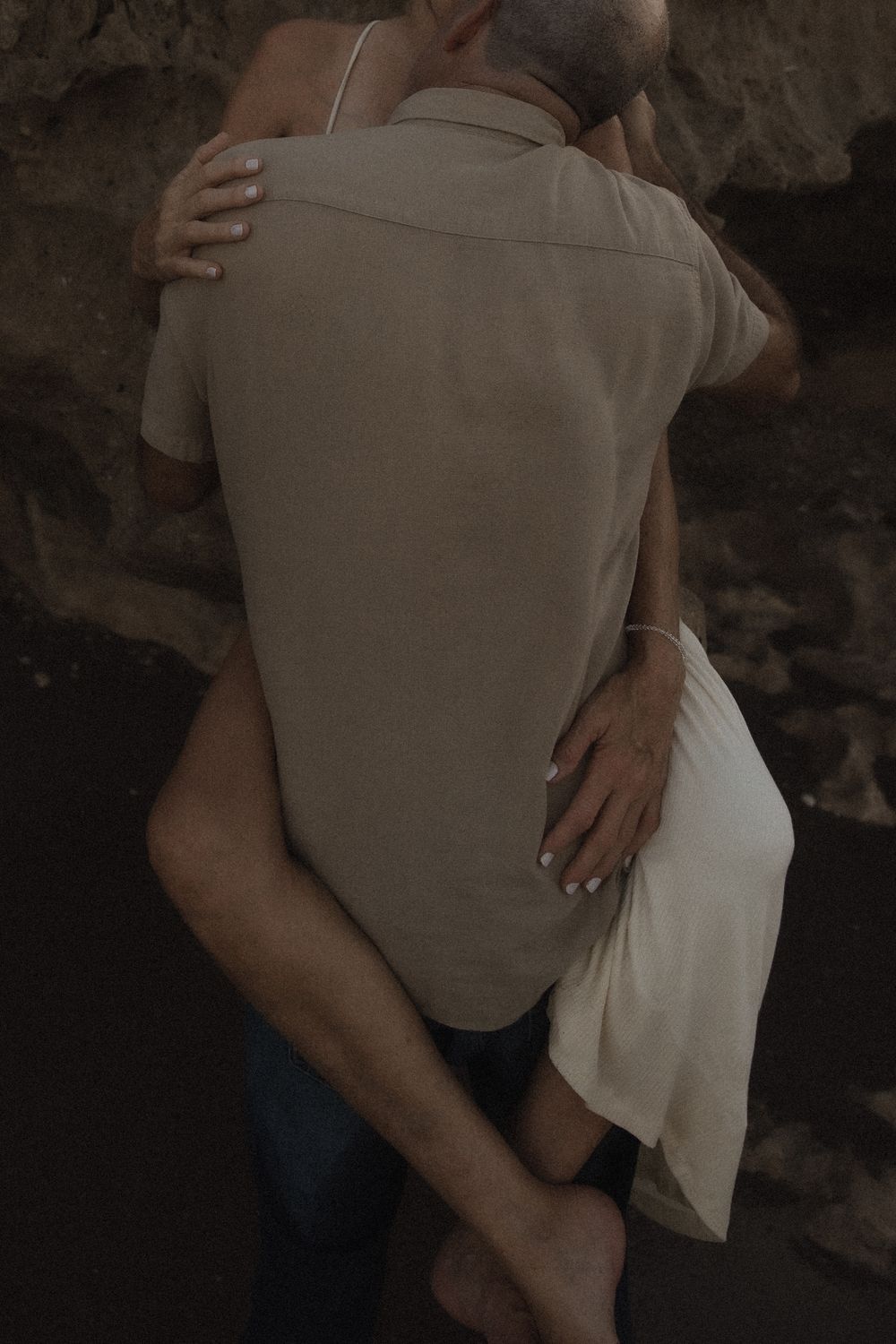 Intimate couple embraces in moody lighting, with one person wearing a beige shirt and the other in white clothing.