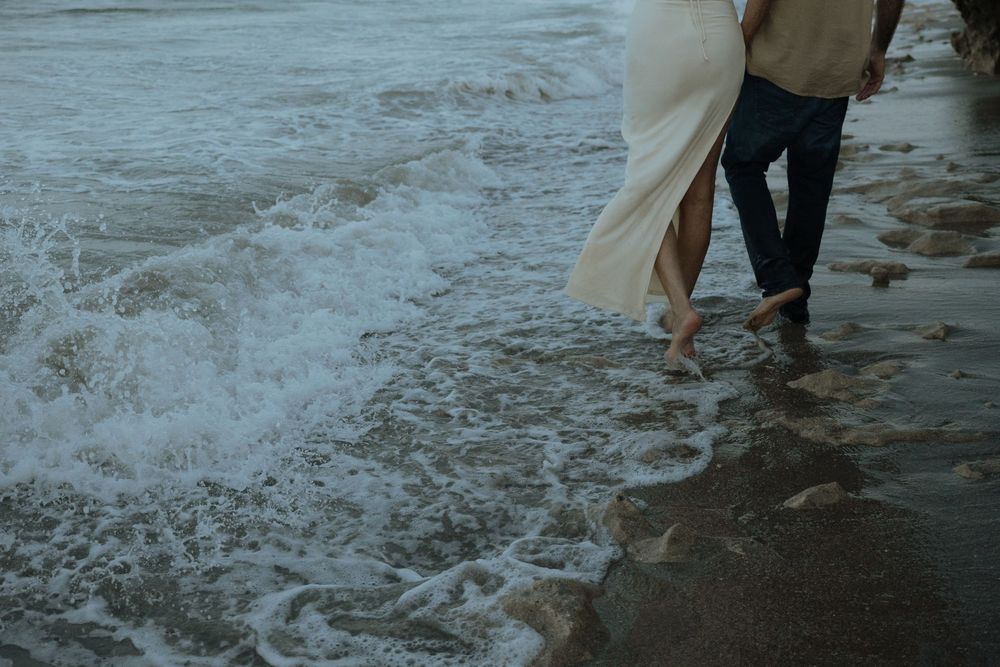 Couple walking barefoot along the beach shore as waves splash against their feet creating water patterns in the sand.