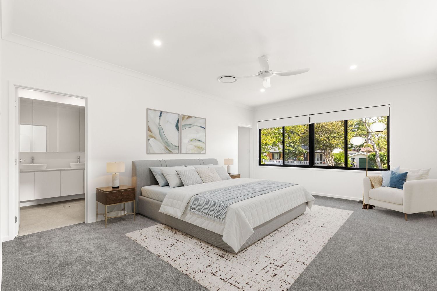 Spacious master bedroom with grey carpet, ceiling fan, large window, ensuite access, and neutral contemporary decor.