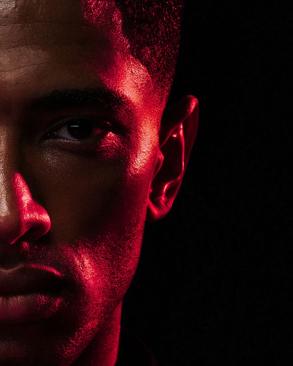 Dramatic portrait with half the face illuminated in deep red lighting against a dark background.