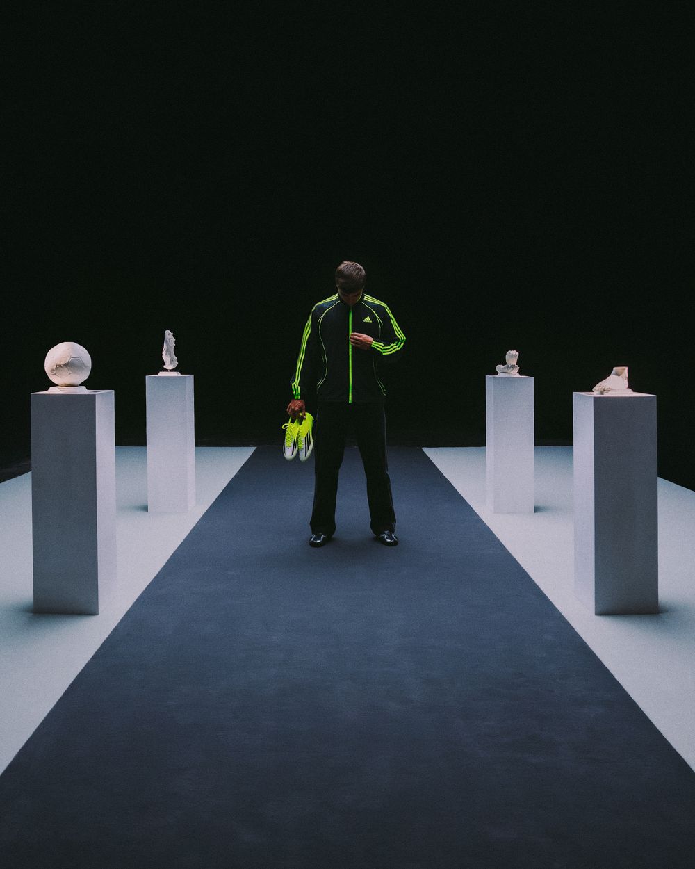 A person walks through a minimalist art installation featuring white geometric pillars against a dark background.