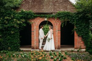 A couple shares a romantic moment in front of a brick archway surrounded by lush green ivy.