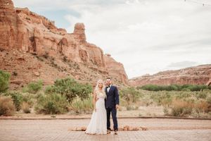 Wedding couple poses in front of towering red rock formations in a scenic desert landscape.