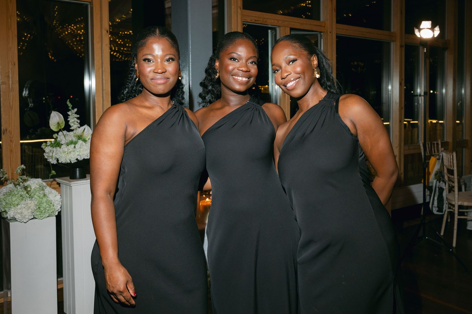 Group of women in elegant black dresses pose together at an evening event.