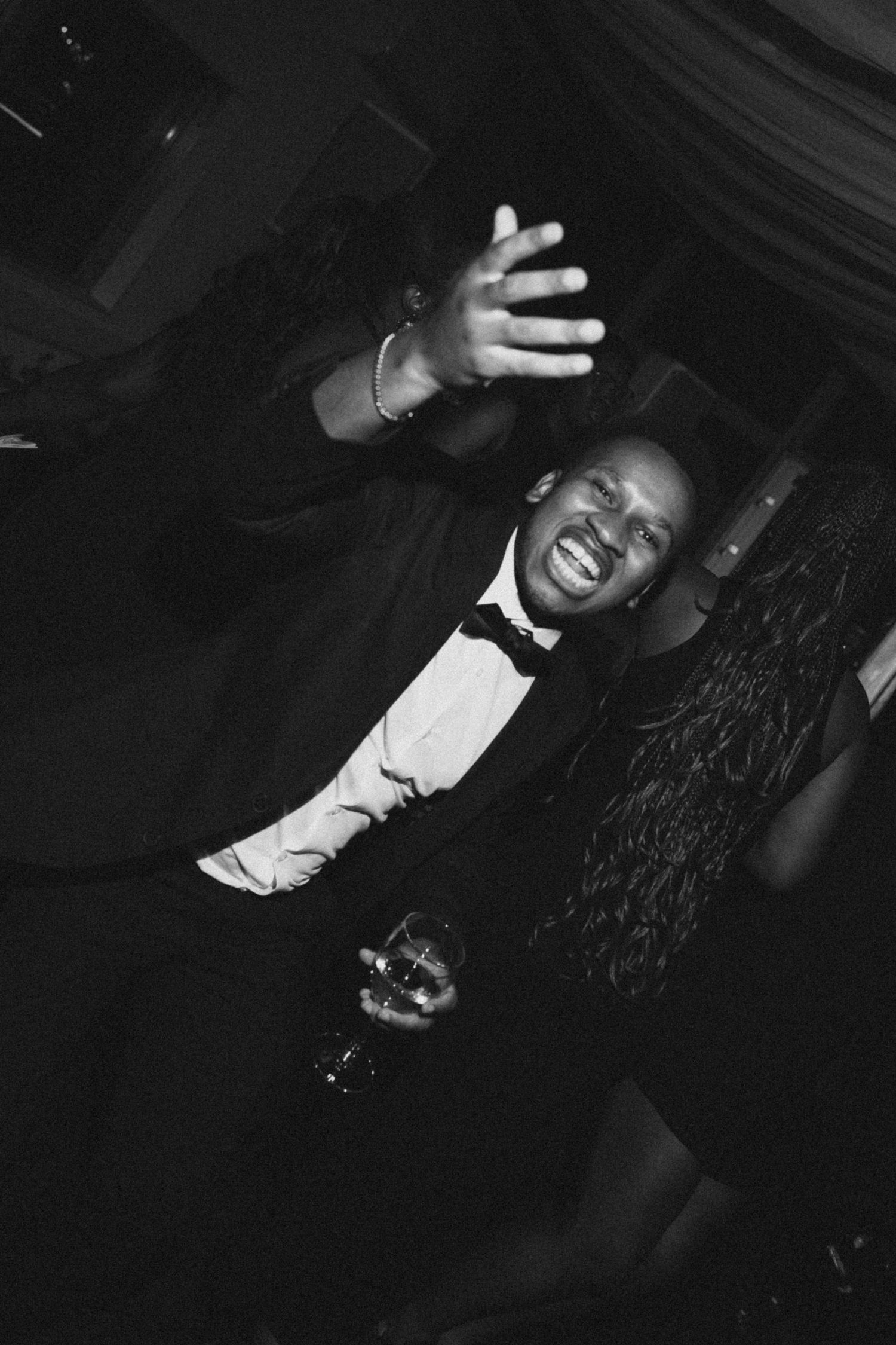 Black and white photo of people laughing and gesturing expressively at a dimly lit social gathering.