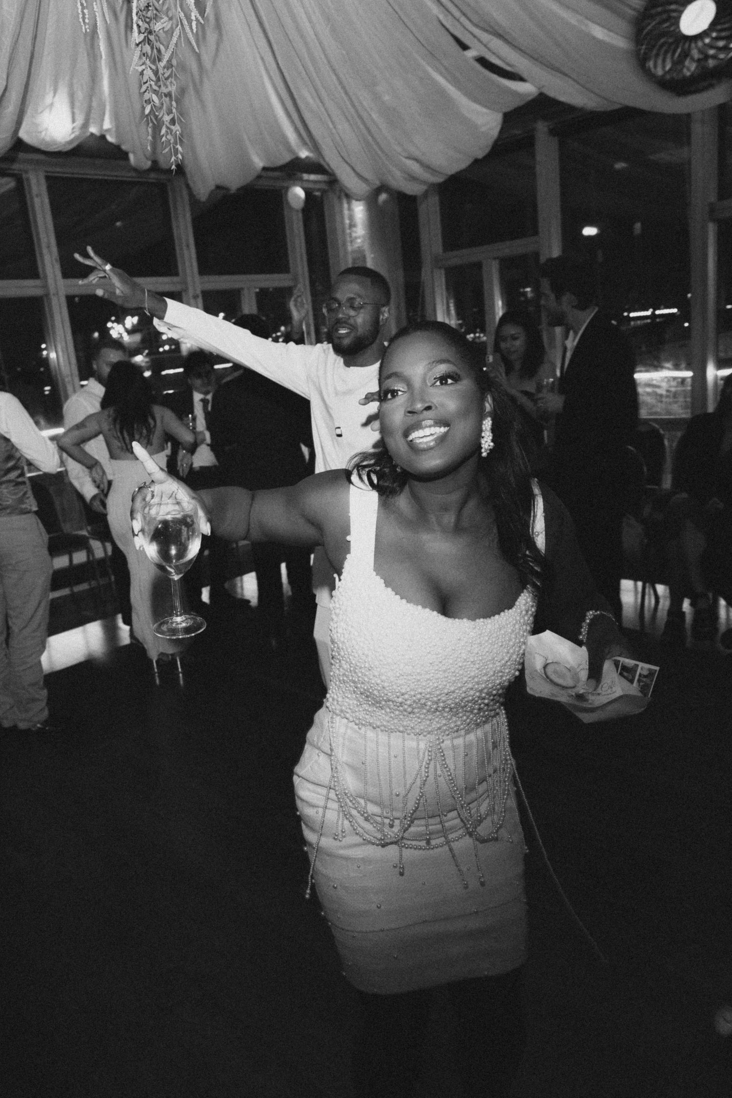 Person in white dress dancing joyfully under draped fabric ceiling at reception.