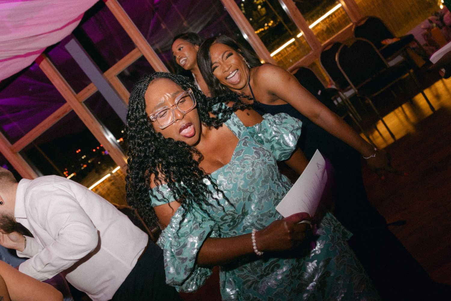 Dancers move energetically on a dance floor illuminated by vibrant pink and purple lighting at an evening event.