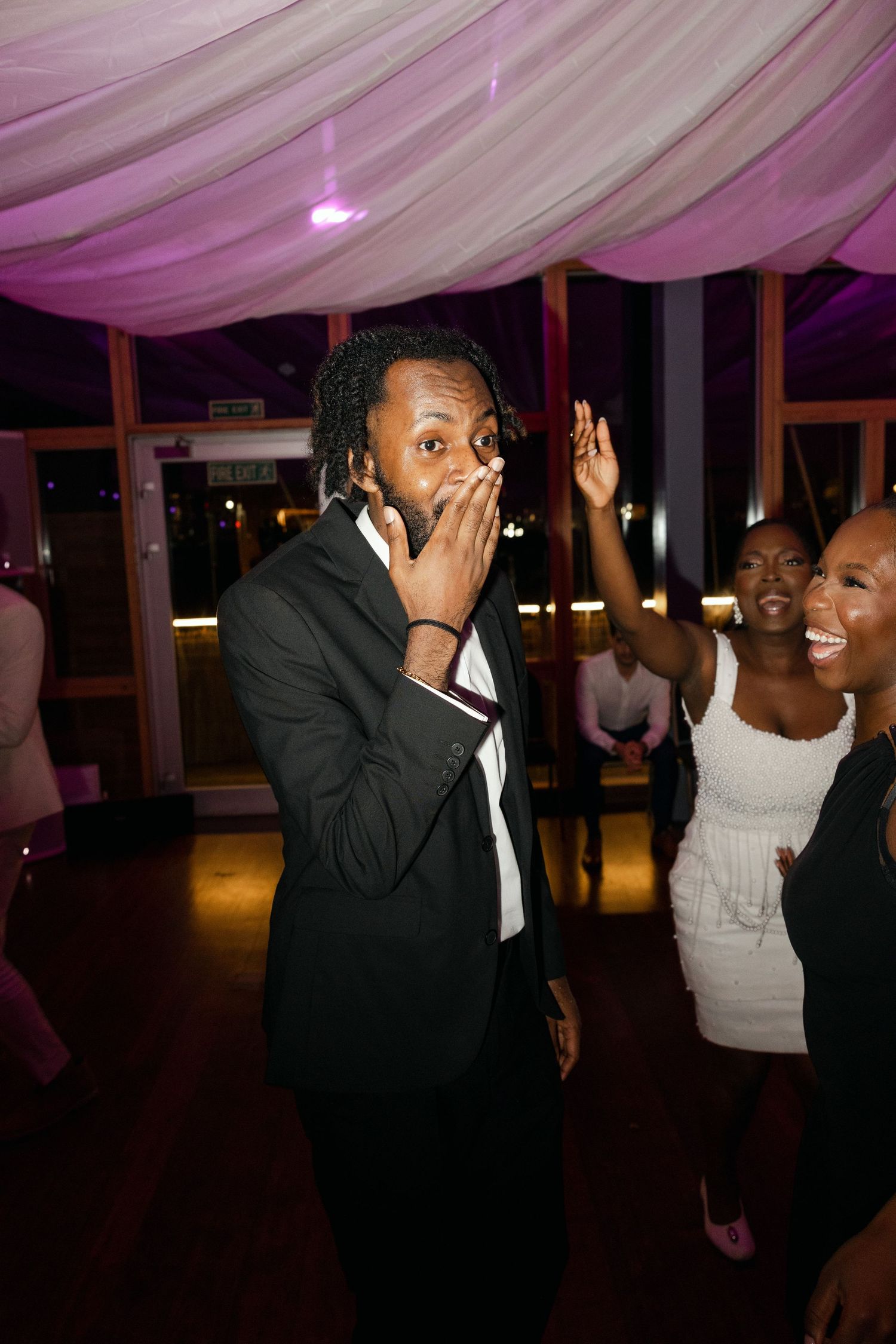 People dancing and enjoying music under pink-lit fabric decor at evening celebration.