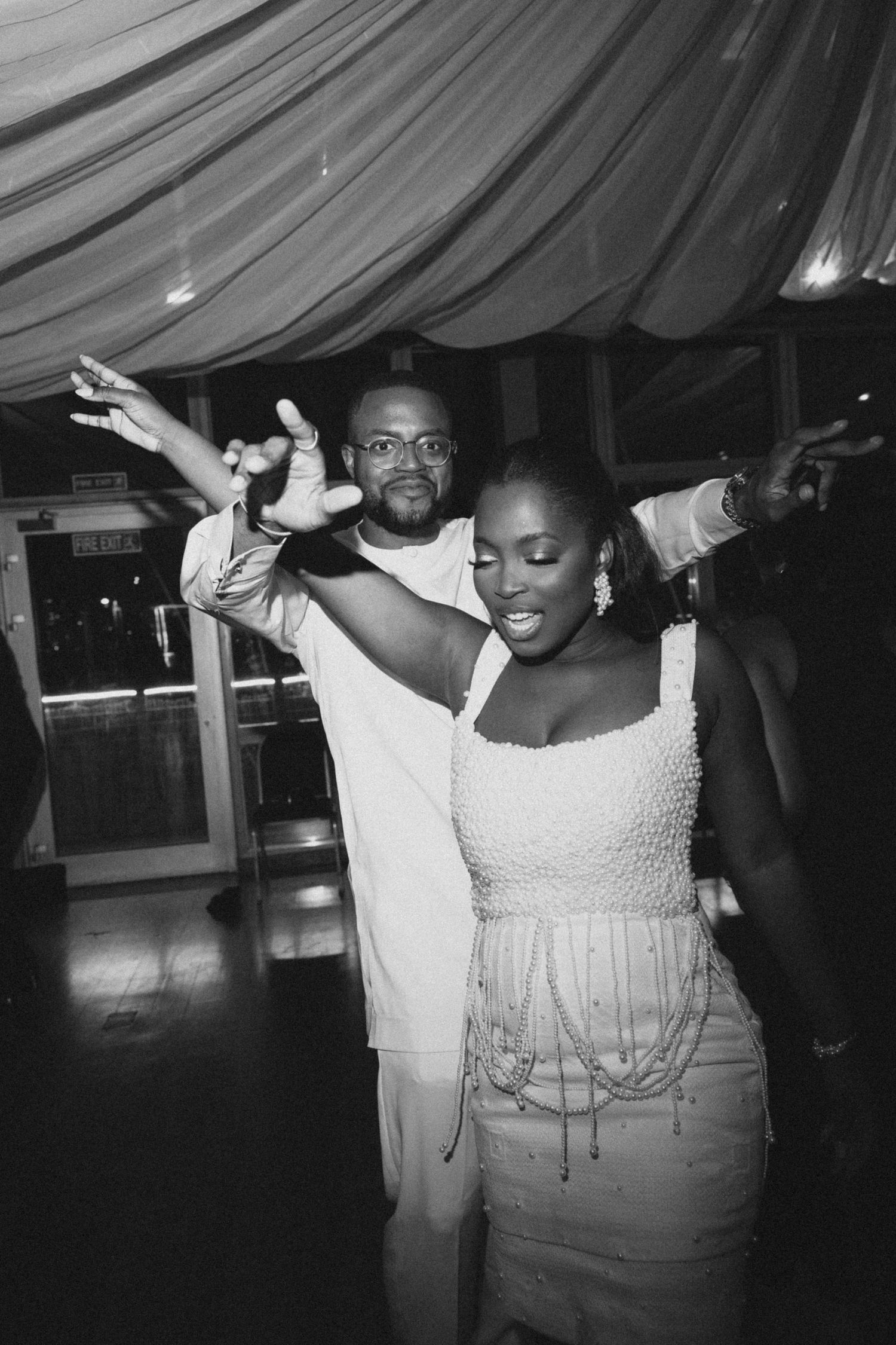 A joyful couple dances together at a wedding reception under draped fabric ceiling decorations.