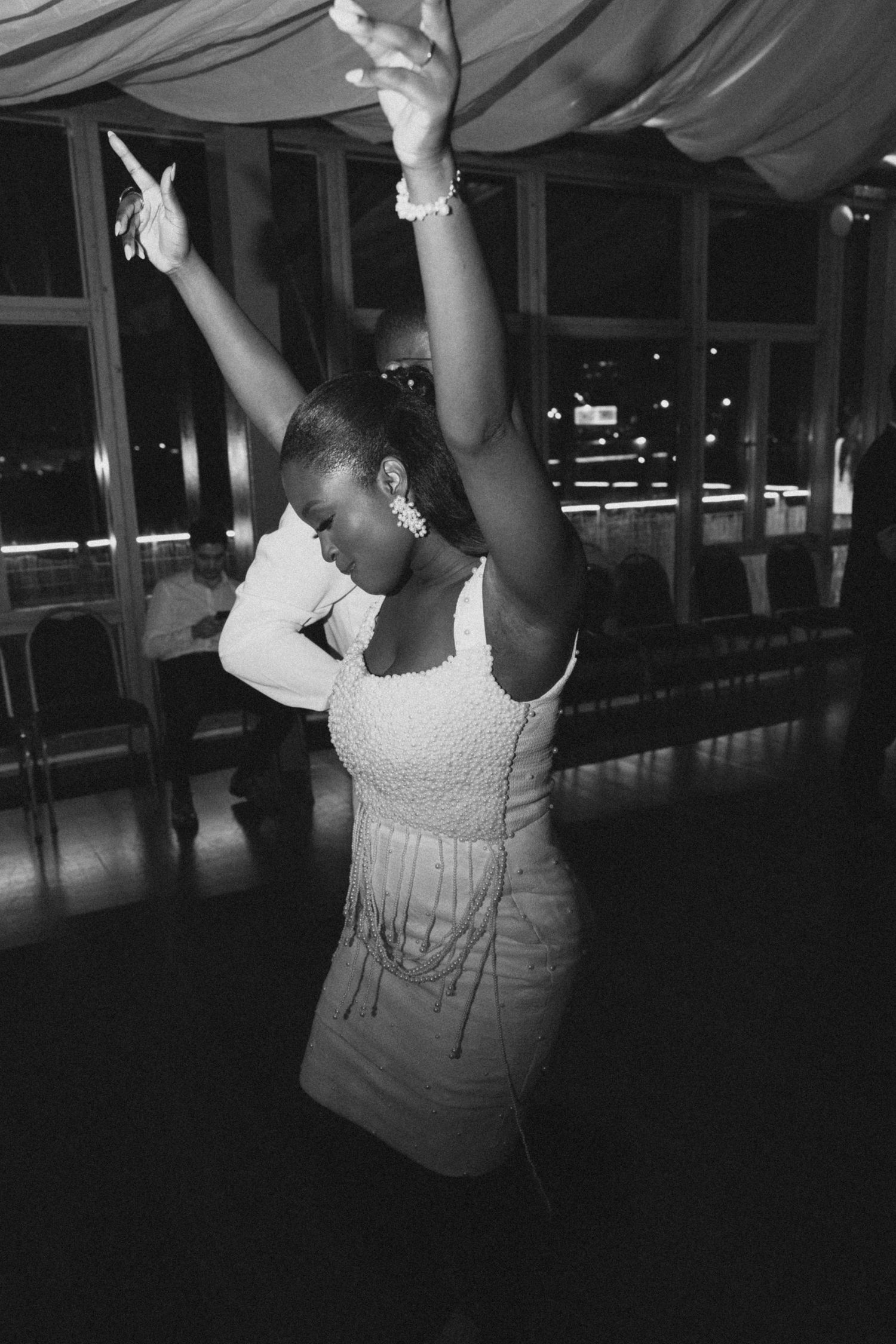 A person in white dancing and raising their hands at an indoor event with draped ceiling decor.