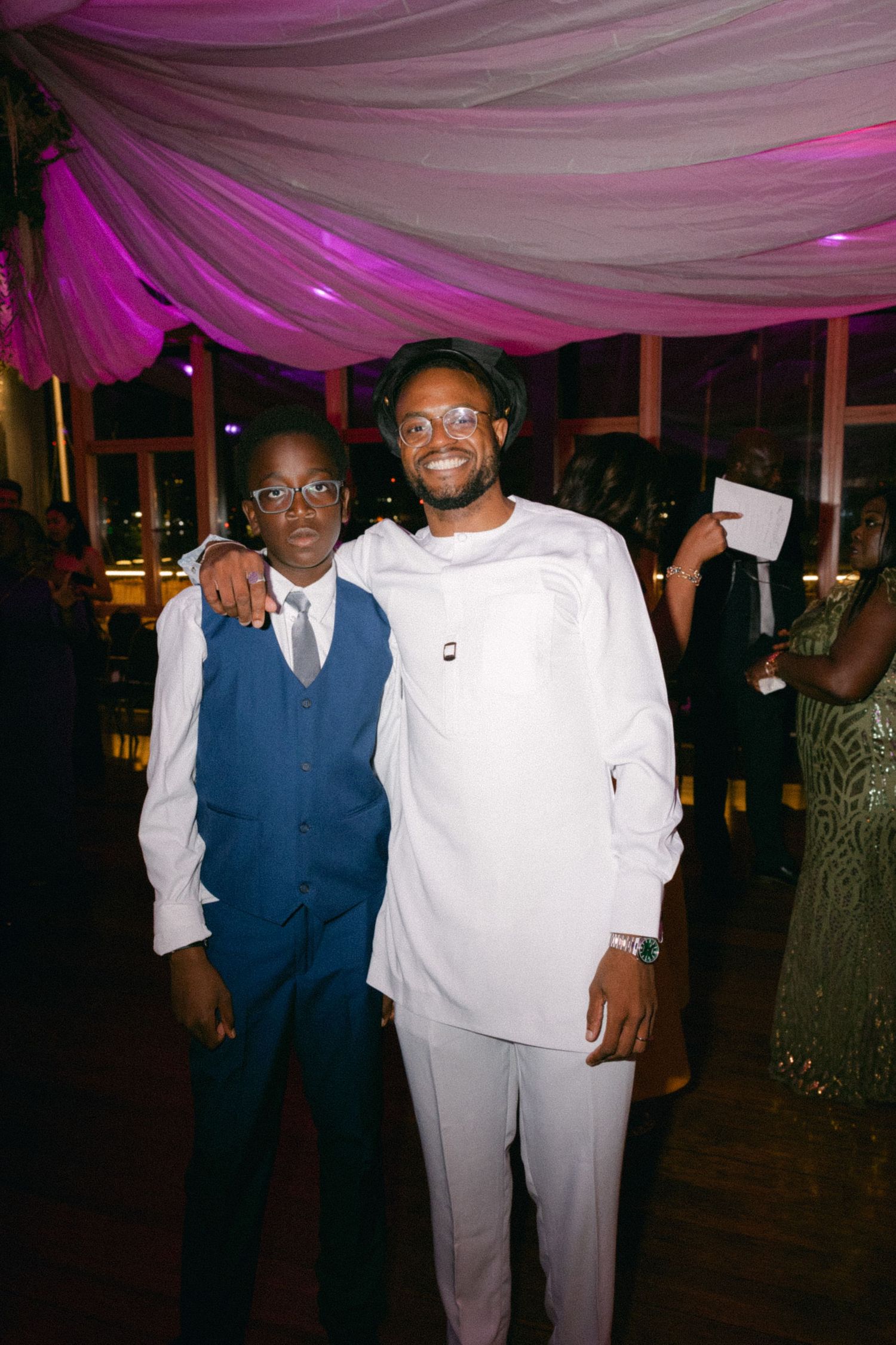 Two people pose together at a formal event under purple and white draped decorations.