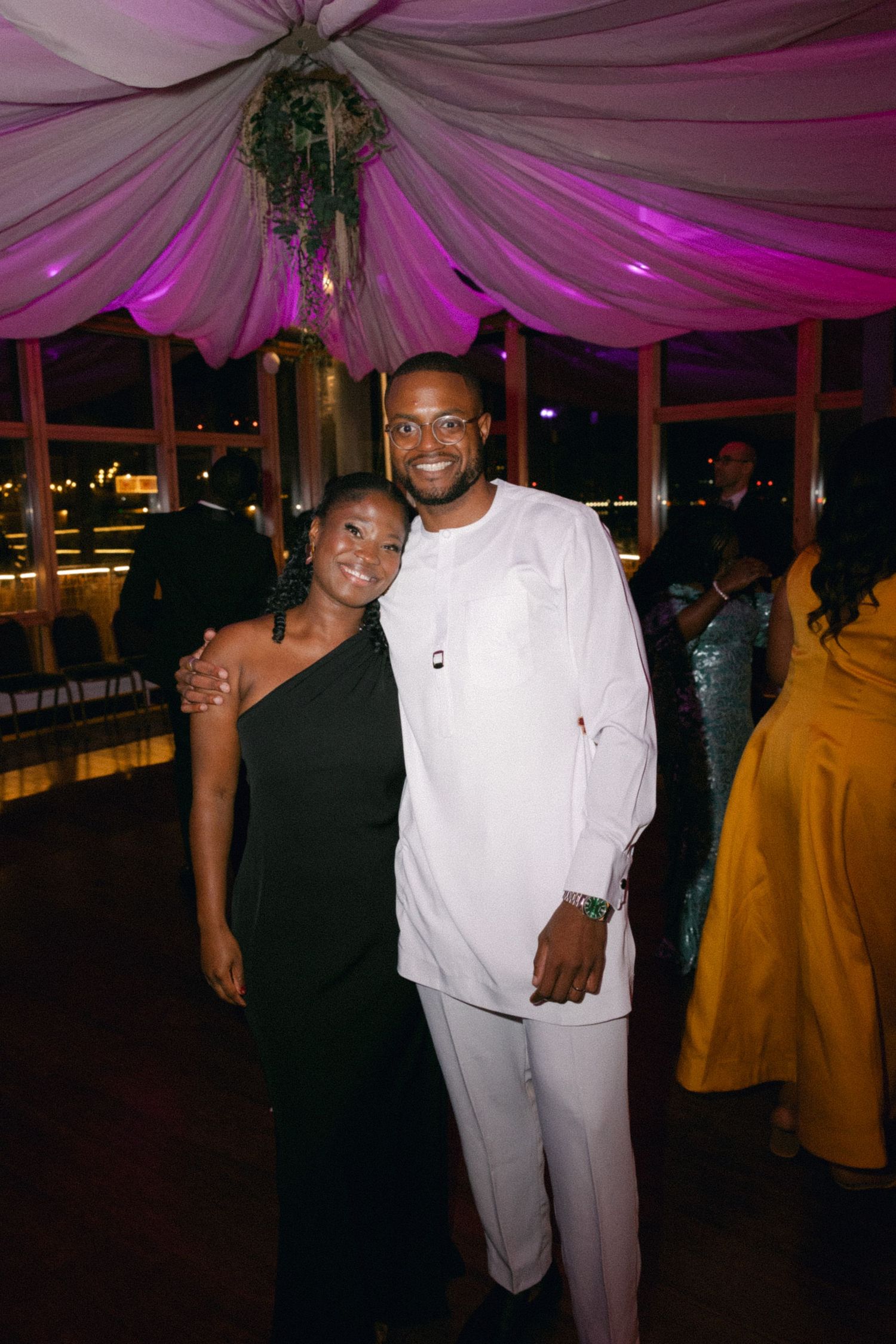 Wedding guests mingling under elegant pink ceiling draping at evening reception.