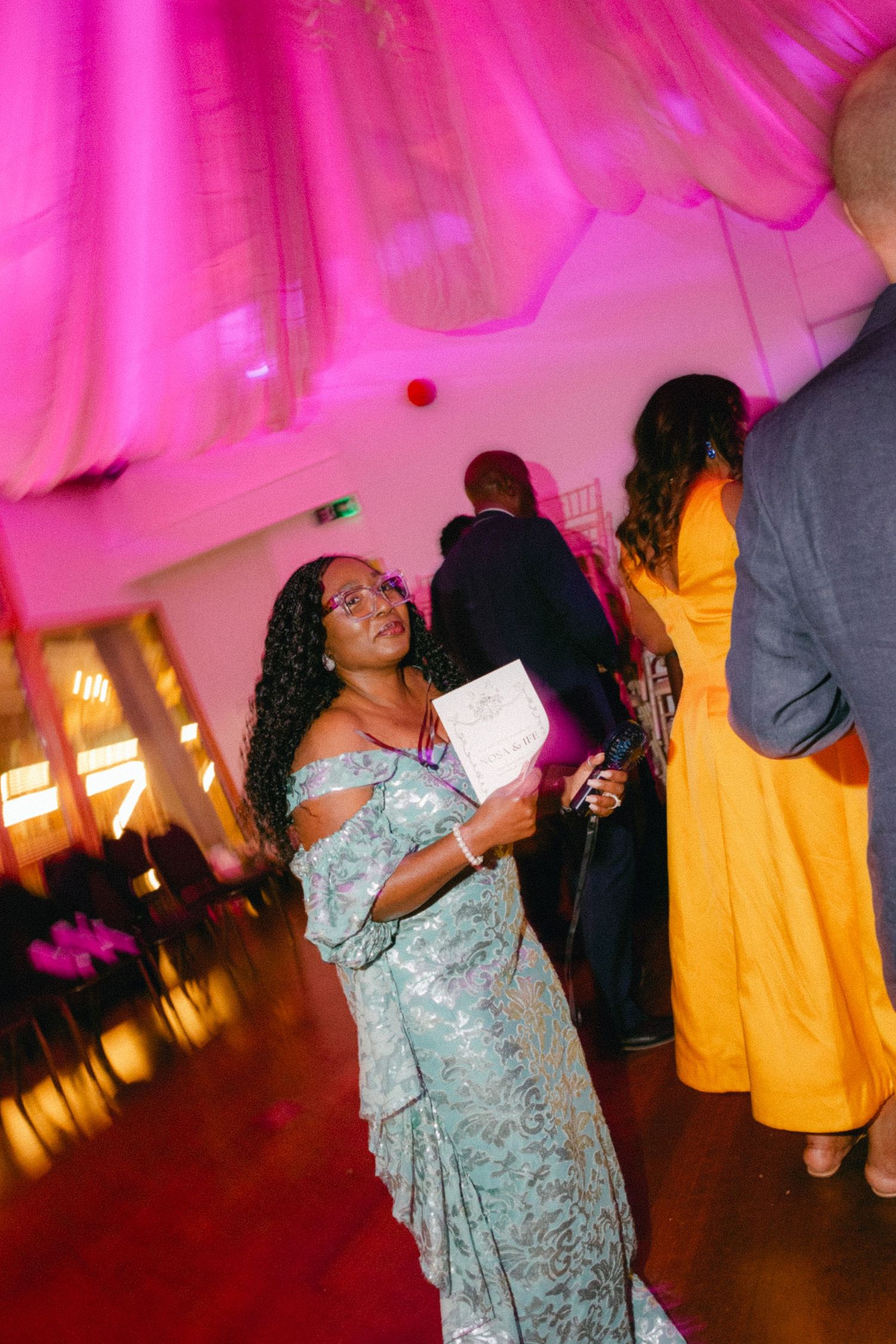 People dancing and celebrating at a party with pink lighting and festive atmosphere.