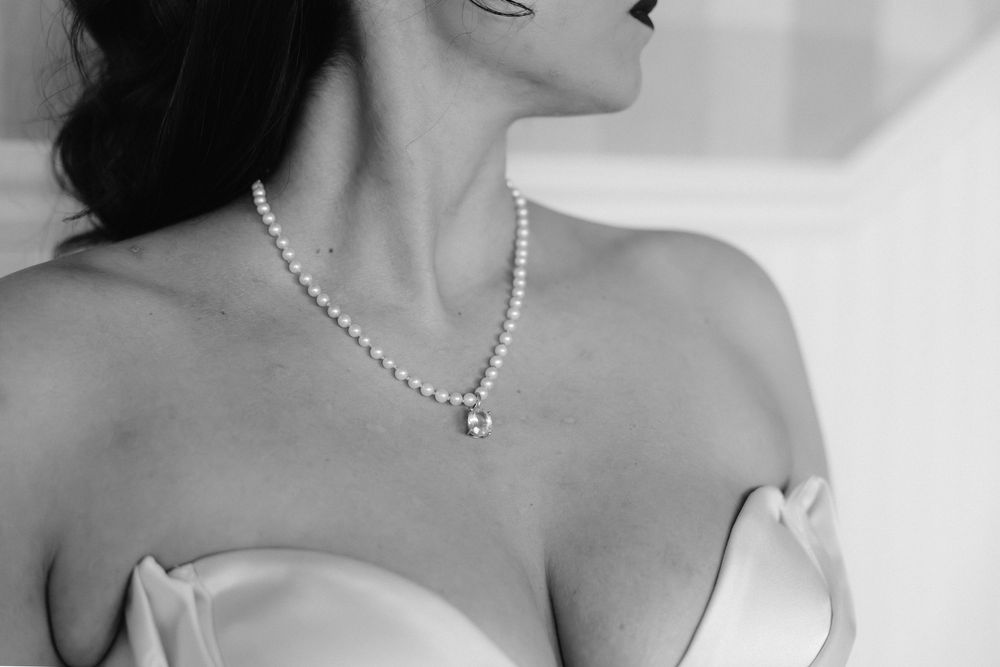 Close-up details of pearl necklaces and strapless gowns at an elegant wedding.