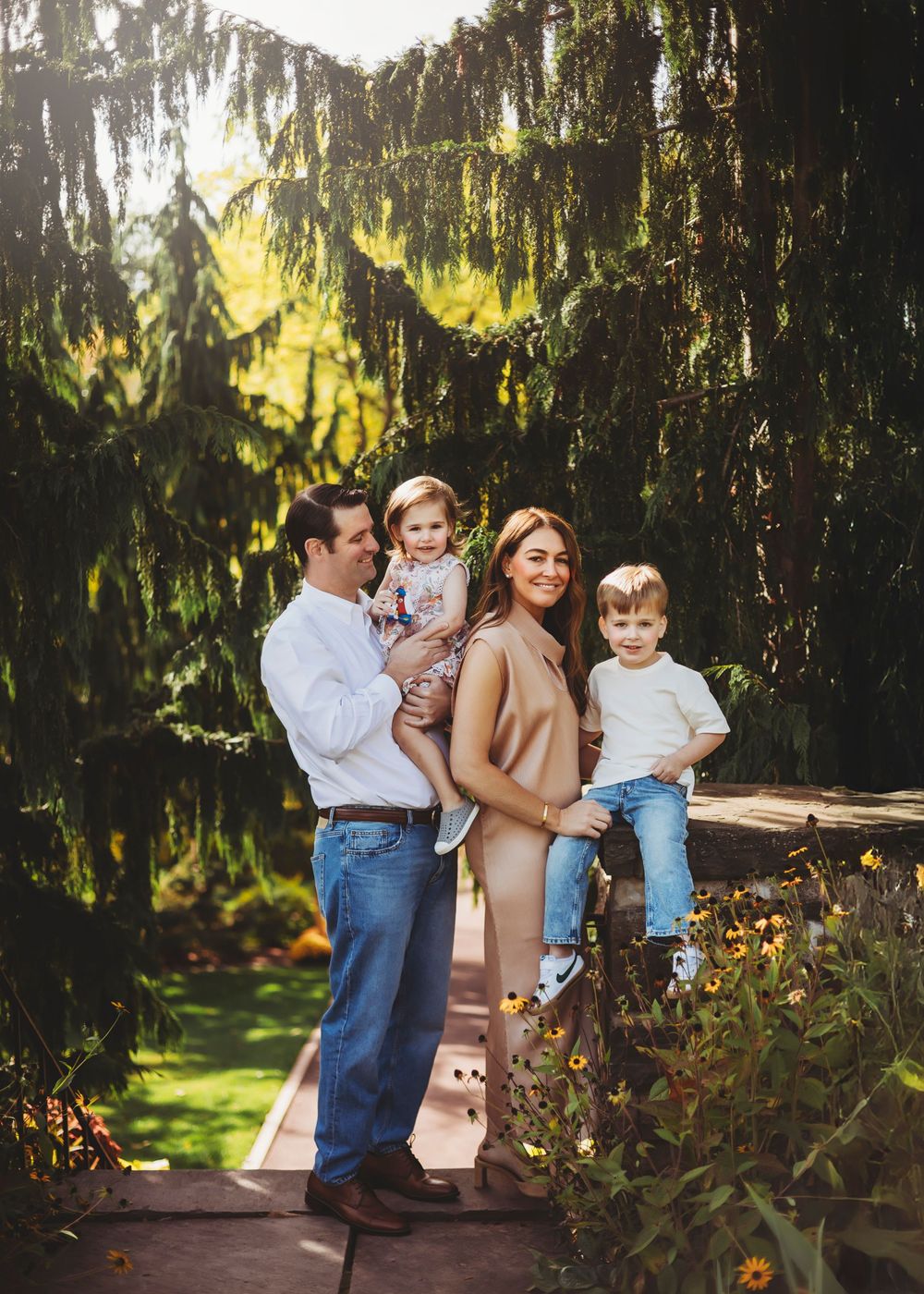 Family portrait session showing loving interactions between parents and children in a garden setting with willow trees.