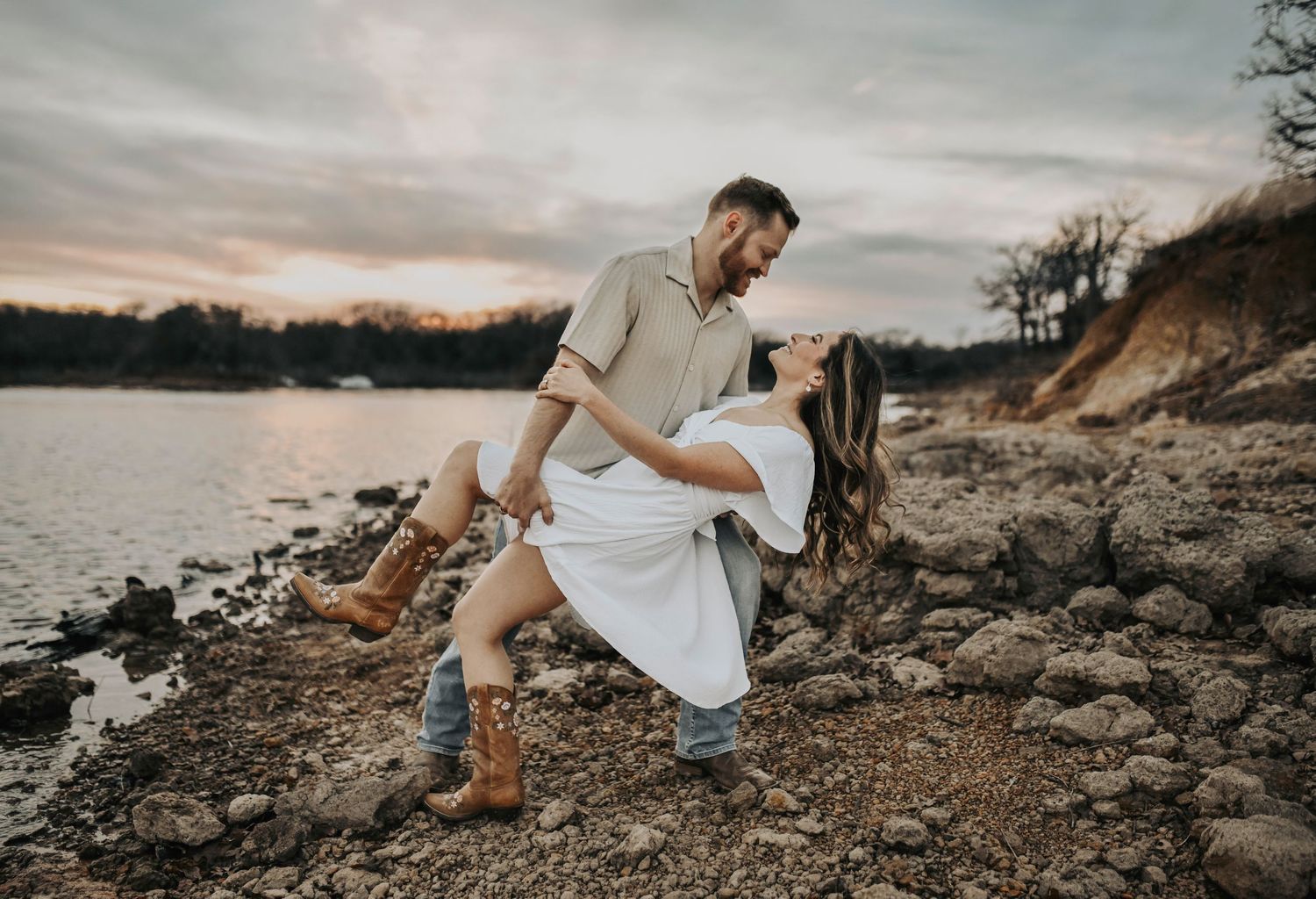 Romantic engagement photo of couple looking at each other along Lake Lewisville shoreline at sunset
