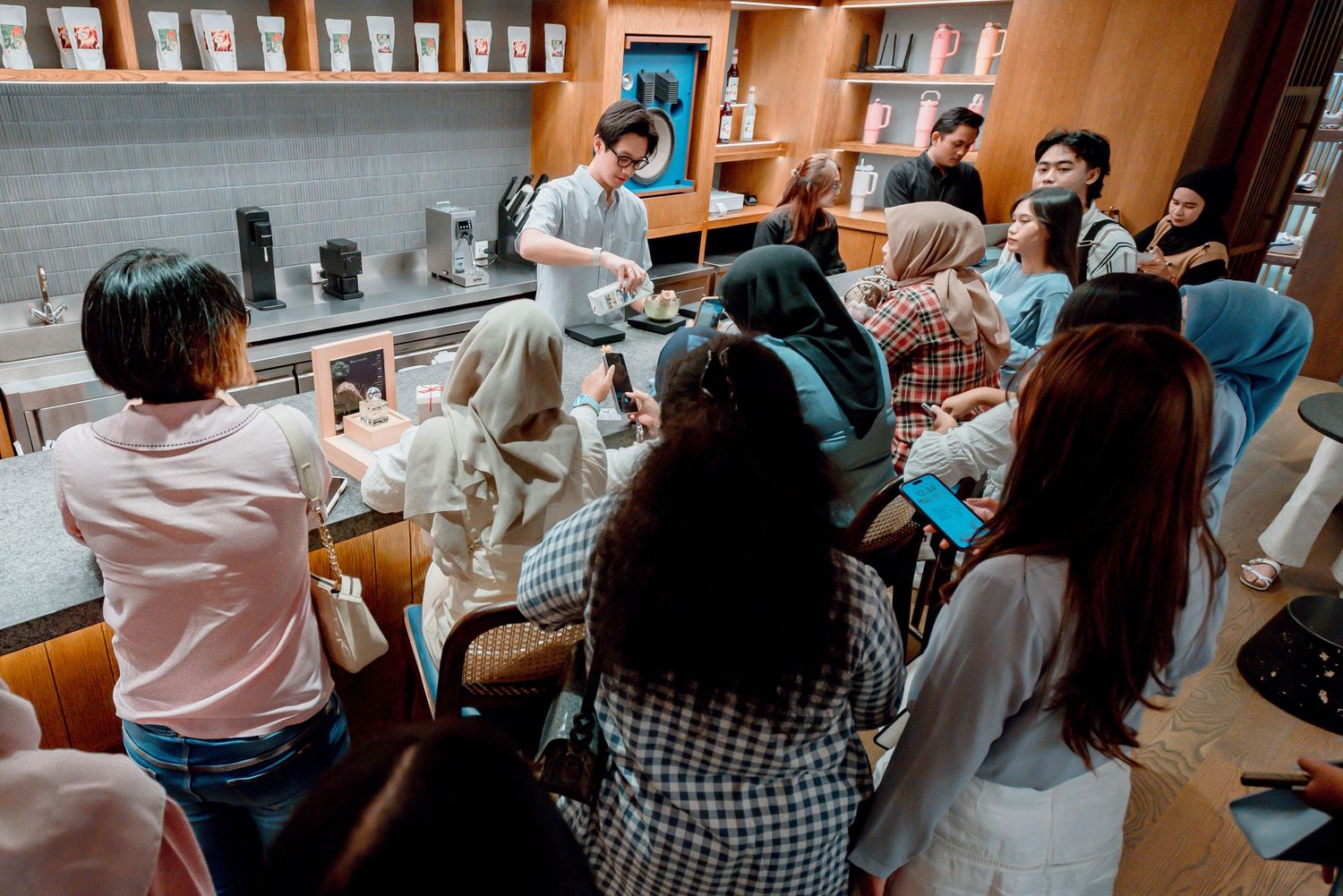 Students sit at tables in a library or study room while working on their assignments.