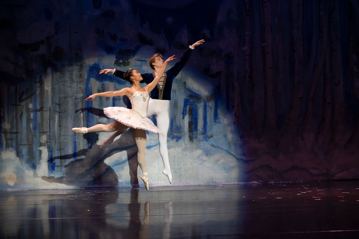 Ballet dancers perform a series of graceful leaps and poses in dramatic lighting against a dark stage background.
