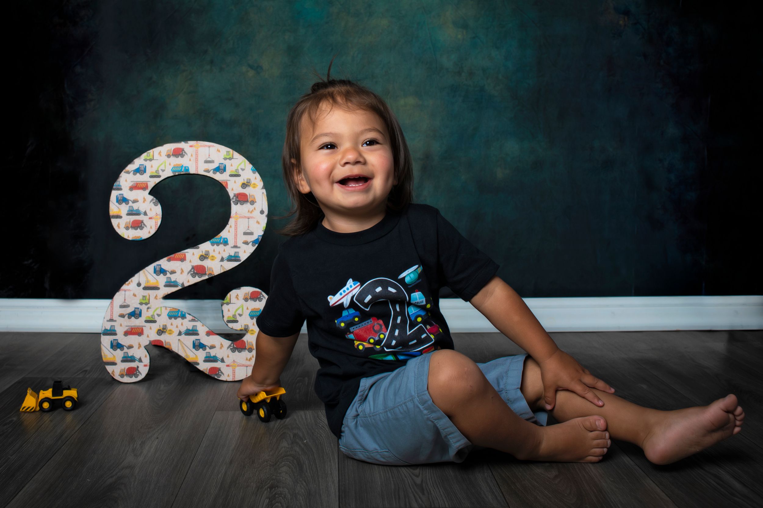A child sits with a birthday number 3 decoration and colorful bubbles against a dark blue background.