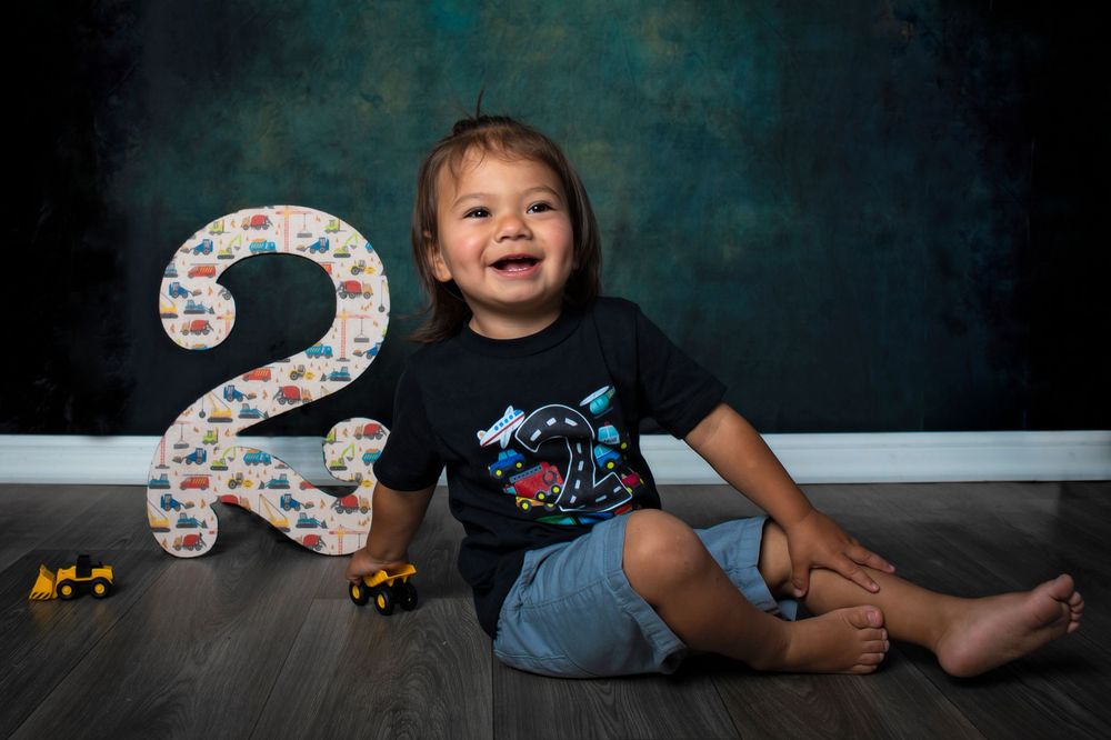 A child sits with a birthday number 3 decoration and colorful bubbles against a dark blue background.