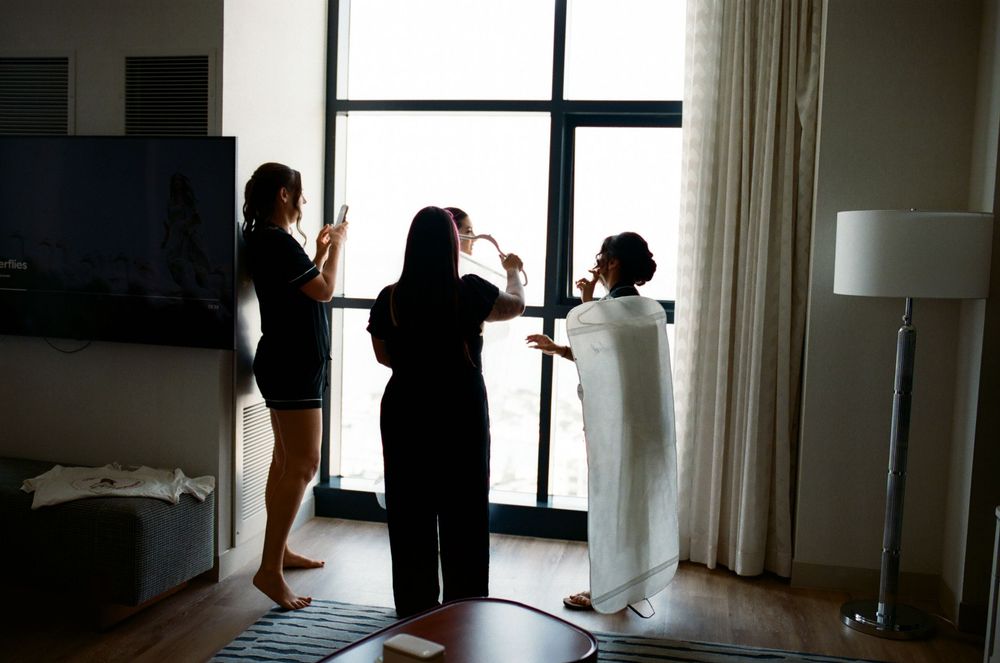 Three people stand by a large window in a hotel room during what appears to be a preparation or getting ready moment.