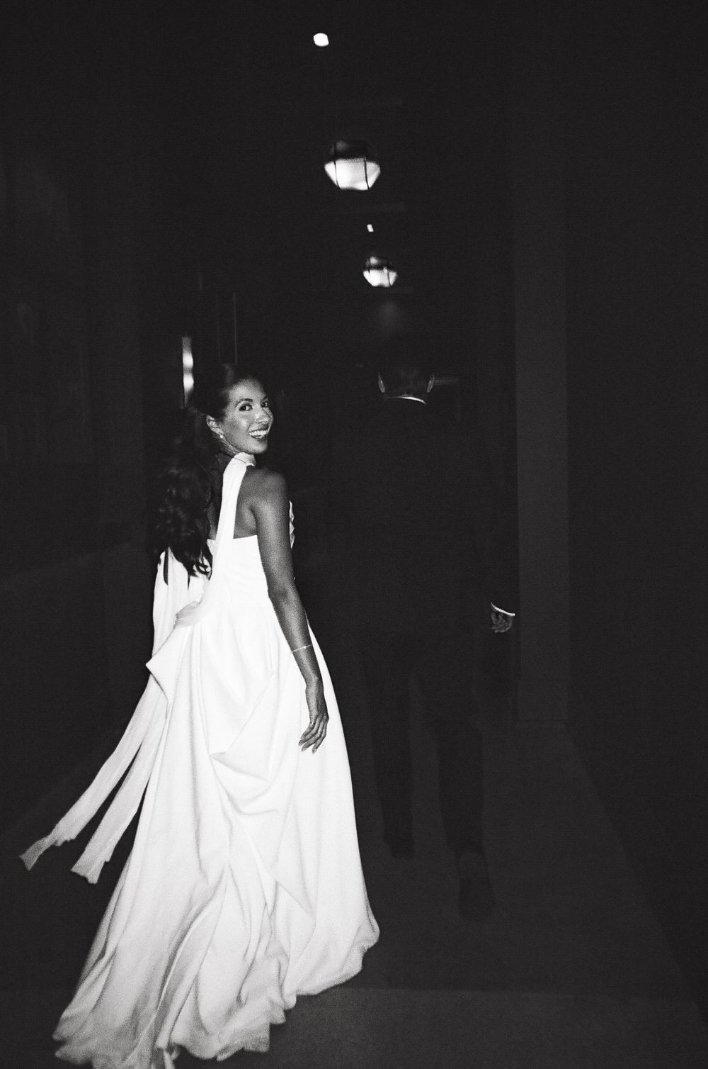 A person wearing a flowing white dress walks through a dark space in a series of black and white photographs.