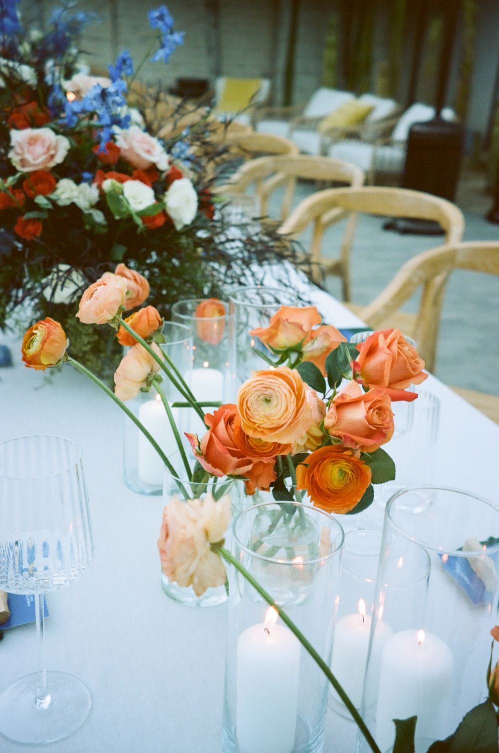 Orange ranunculus flowers in glass vases decorate elegant table settings with white linens and glassware.