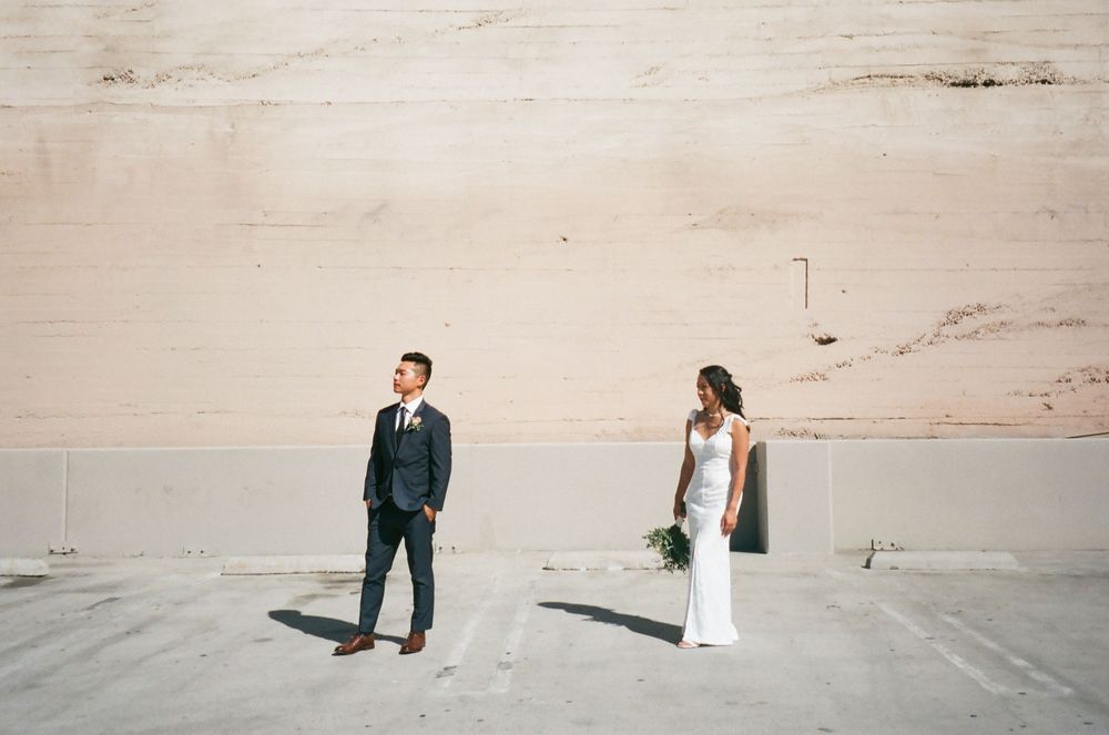 A couple in wedding attire walks along a serene beach shoreline during a romantic sunset photo session.