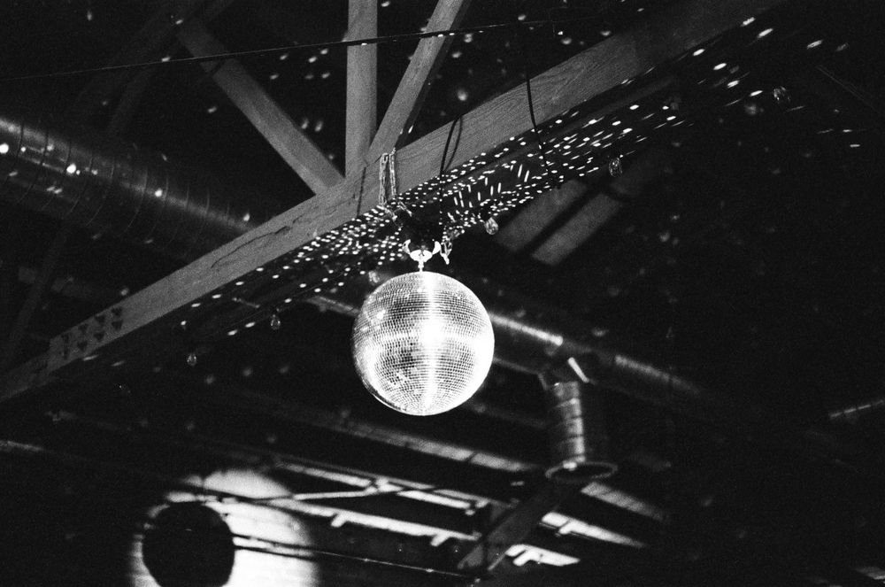 A shiny disco ball reflects light onto a dark ceiling, creating a sparkling nightclub atmosphere.