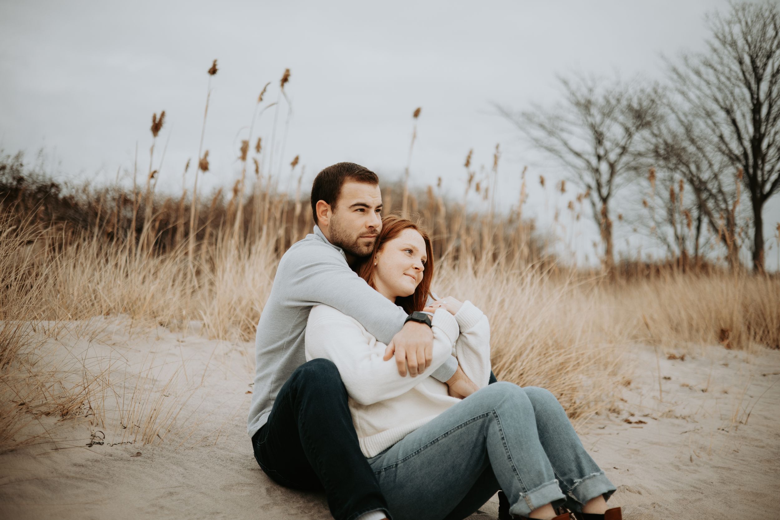 Couple relaxing together in tall autumn grass during golden hour photoshoot.