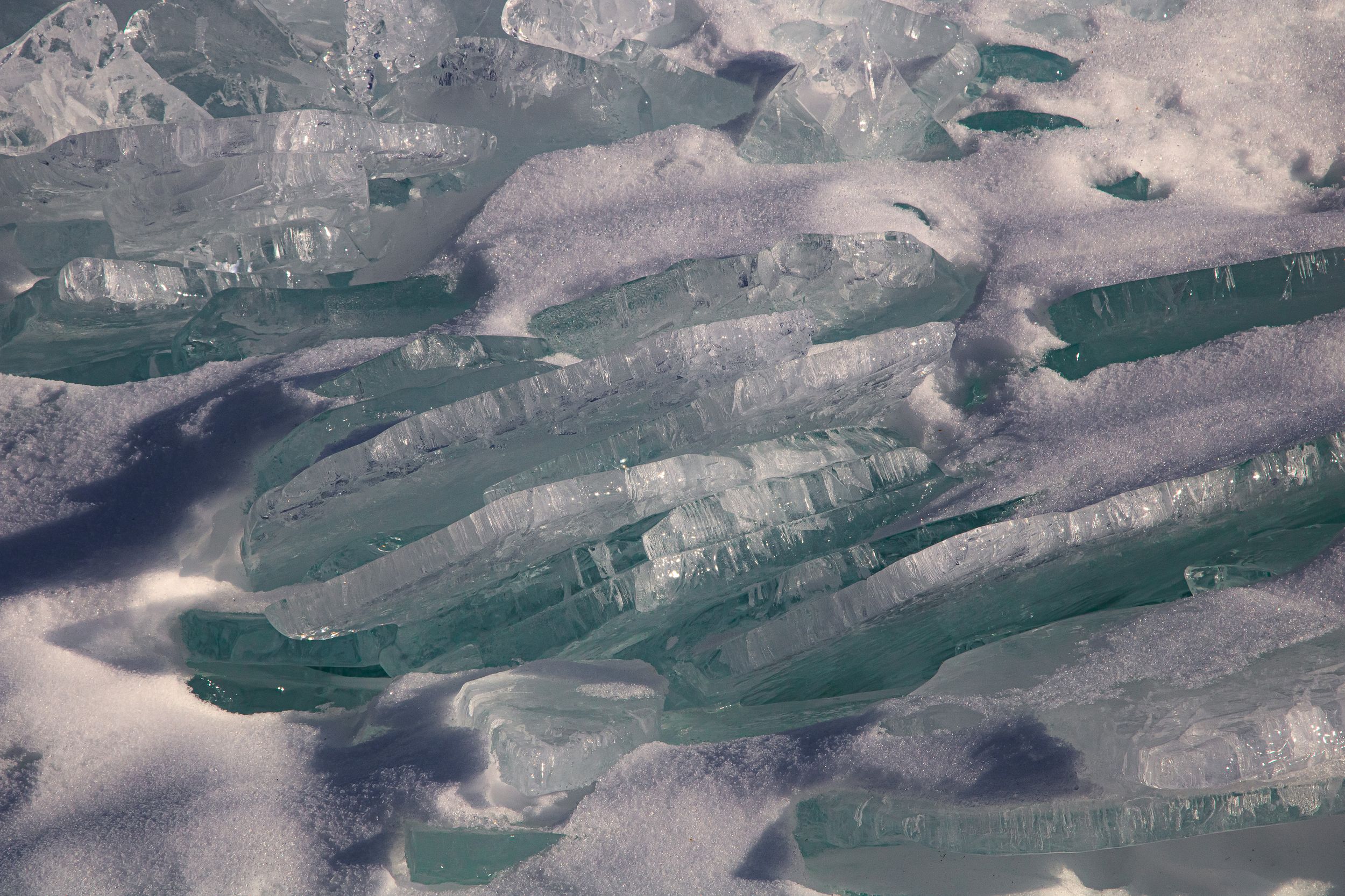Close-up view of cracked blue-green ice formations with crystalline patterns and textures.