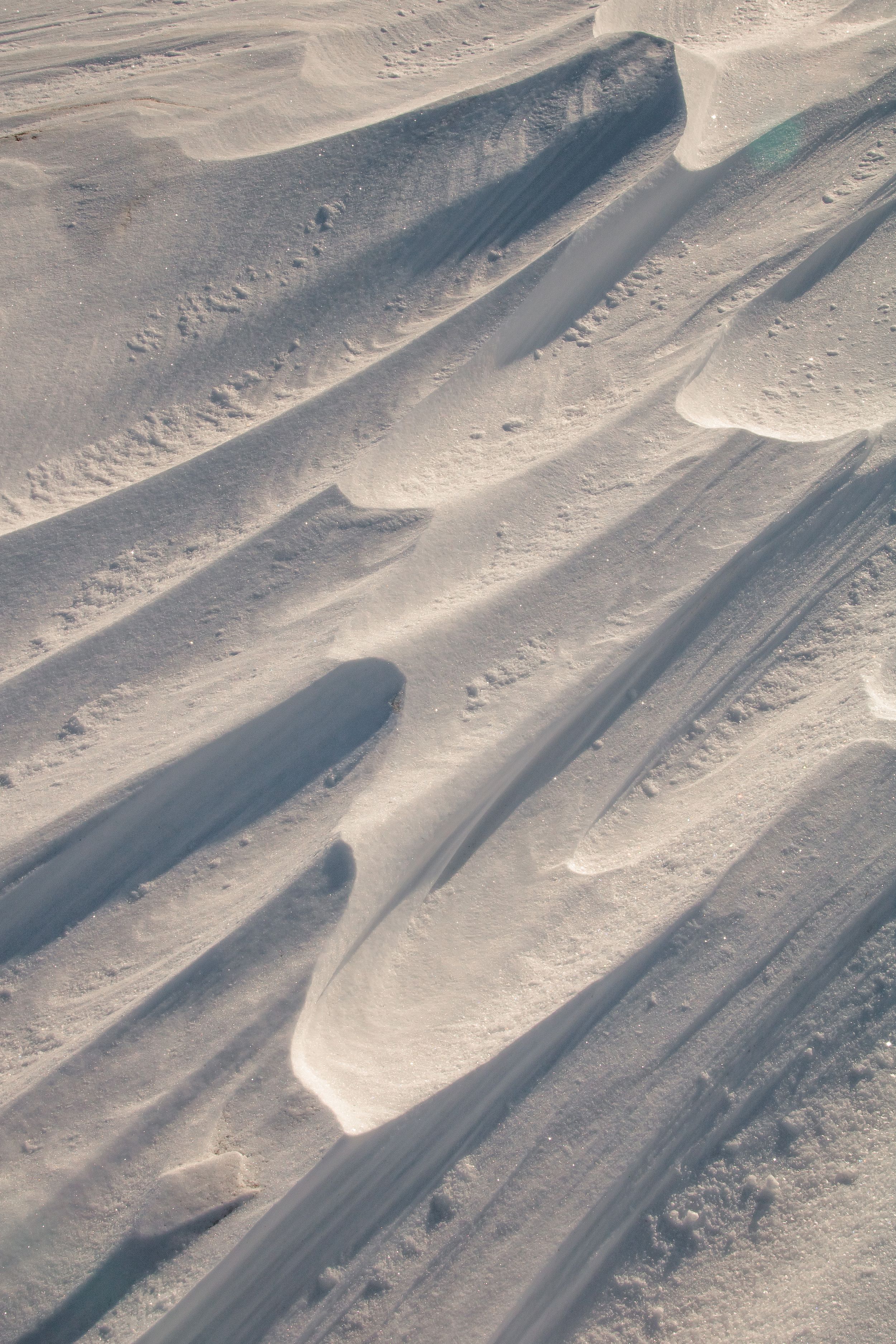 Aerial view of sand dunes with dramatic shadows creating rippling patterns across the desert landscape.