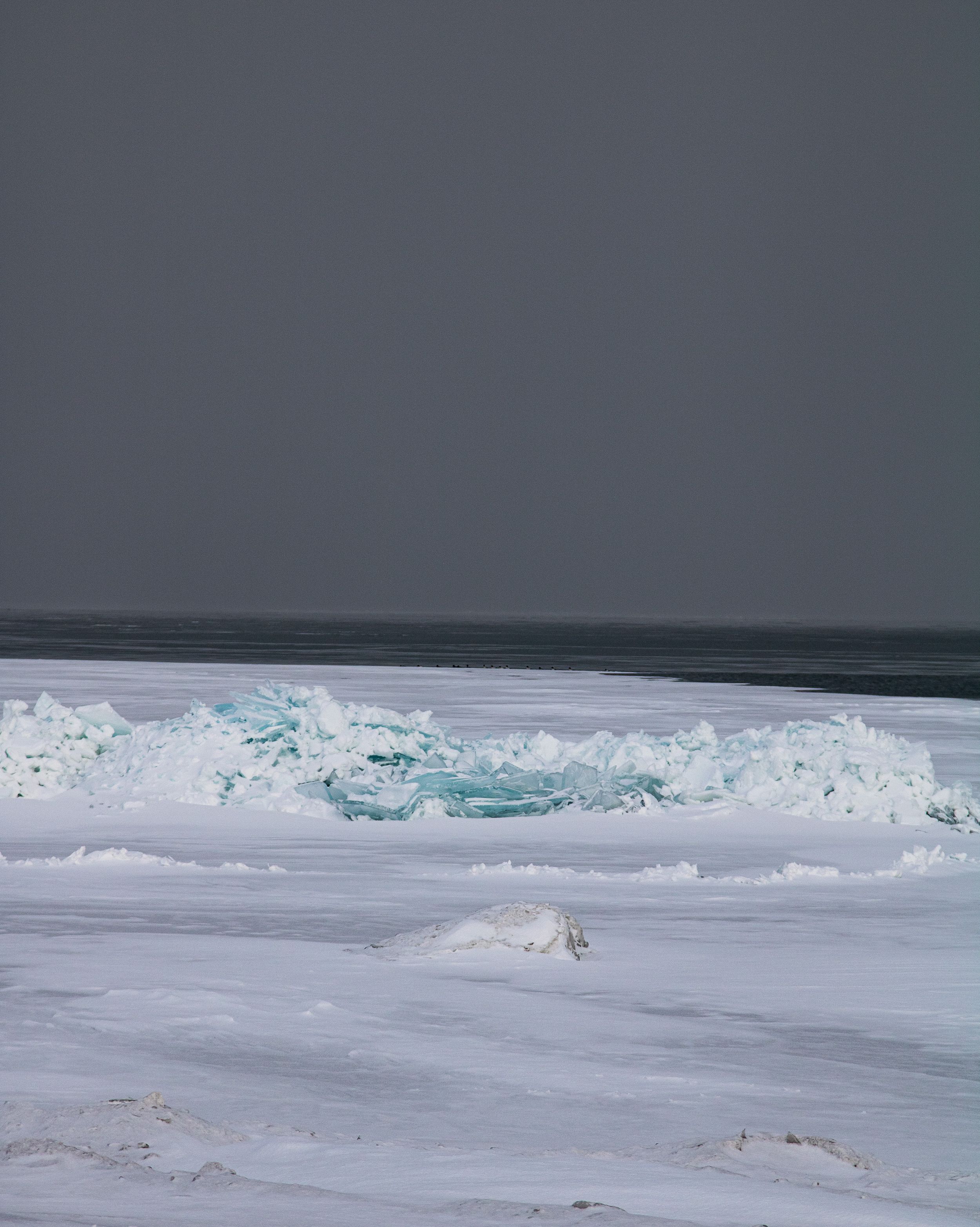Dramatic ocean waves crash against a snowy beach shoreline creating a stark contrast between white foam and dark waters.