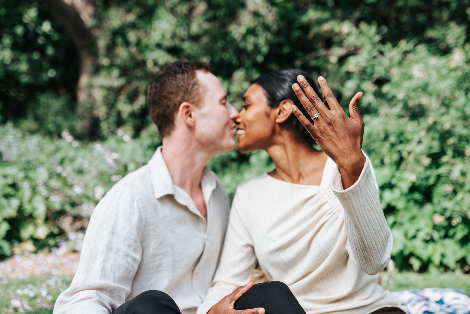 A couple in white outfits shares romantic moments together, showing off her engagement ring during a Melbourne photo session.