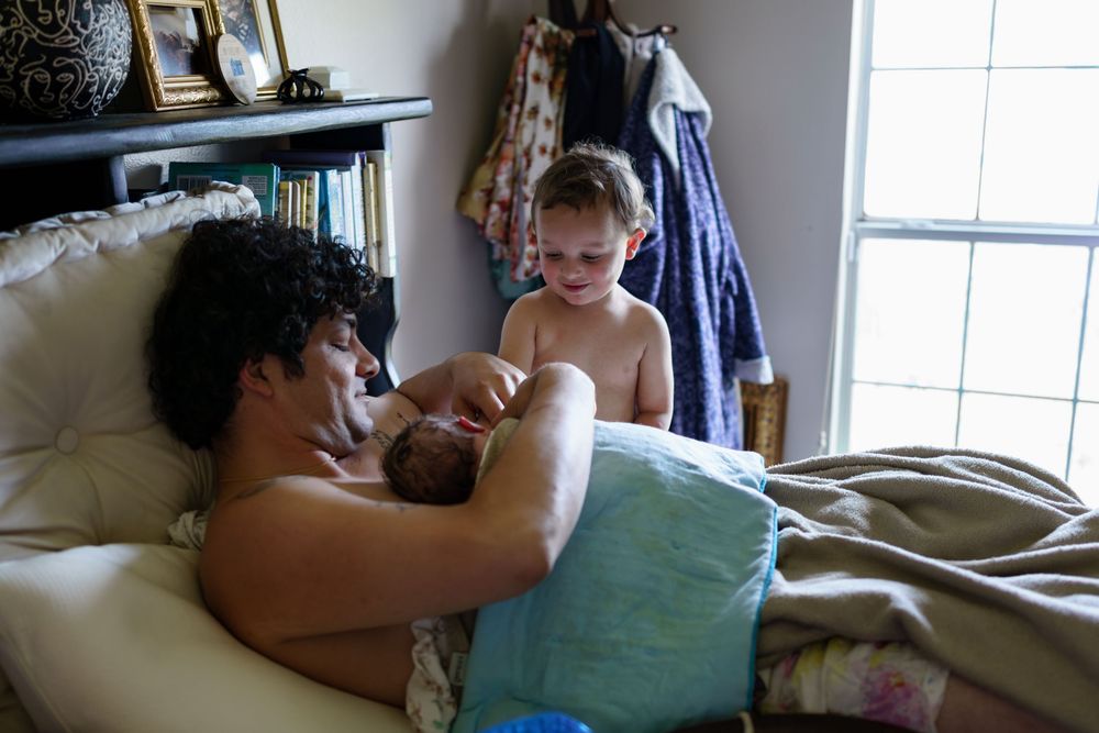 Parent and toddler sharing a tender moment while relaxing in bed near a sunny window.