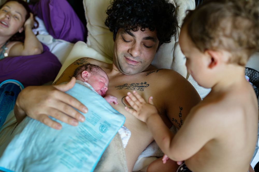 Family resting together on a bed with a baby and toddler in an intimate bonding moment.