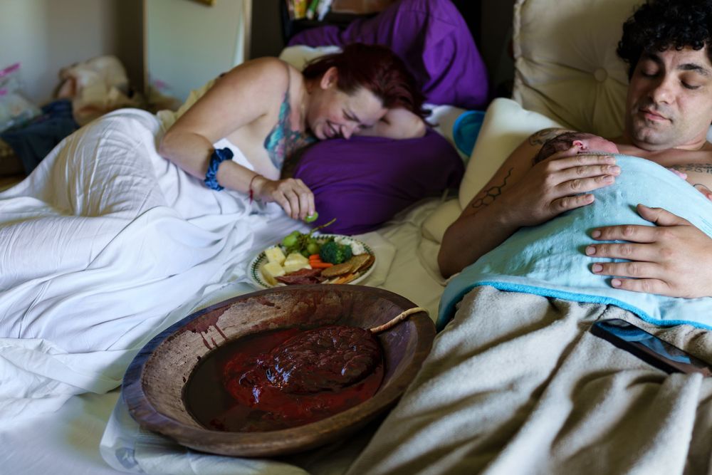 A person resting on white bedding while being comforted by someone in purple clothing.