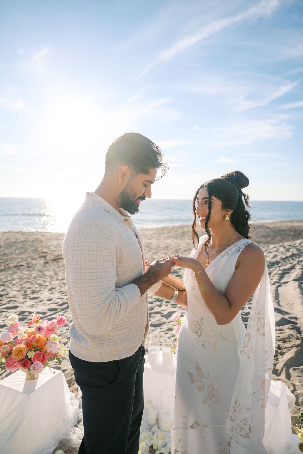 A couple shares an intimate moment exchanging rings during their beach wedding ceremony with floral decor.