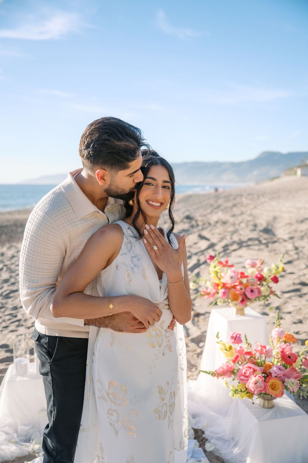 A romantic moment shared between a couple against a desert mountain backdrop with pink and coral floral decorations.