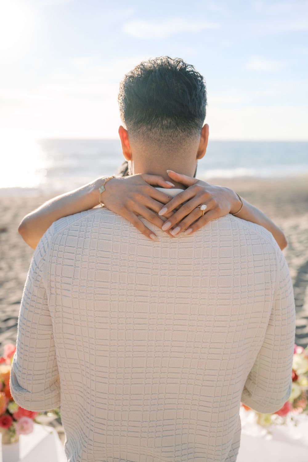 Close-up view of hands tenderly embracing against a white textured shirt with mountains in the background.