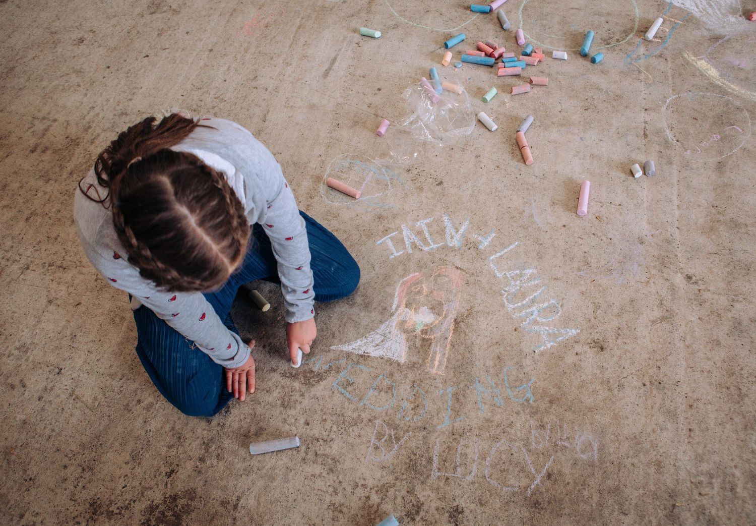 A person in denim pants lies on a concrete floor surrounded by scattered pieces of white chalk.