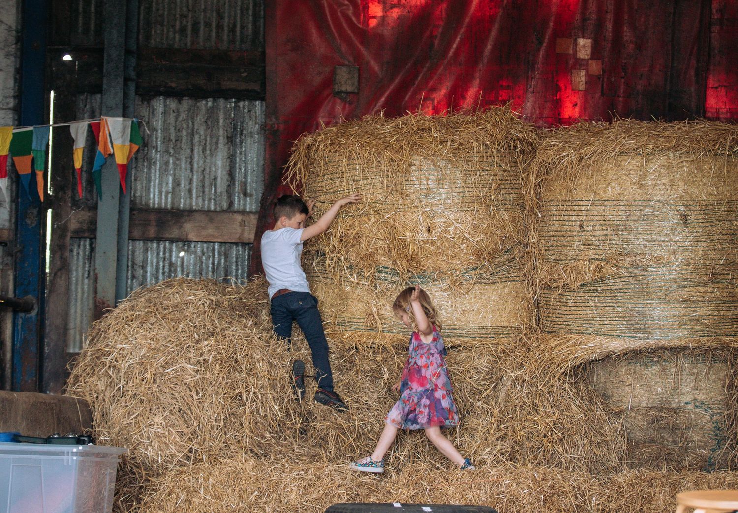 A sequence of action shots showing someone jumping and flipping over hay bales in a barn with red lighting.
