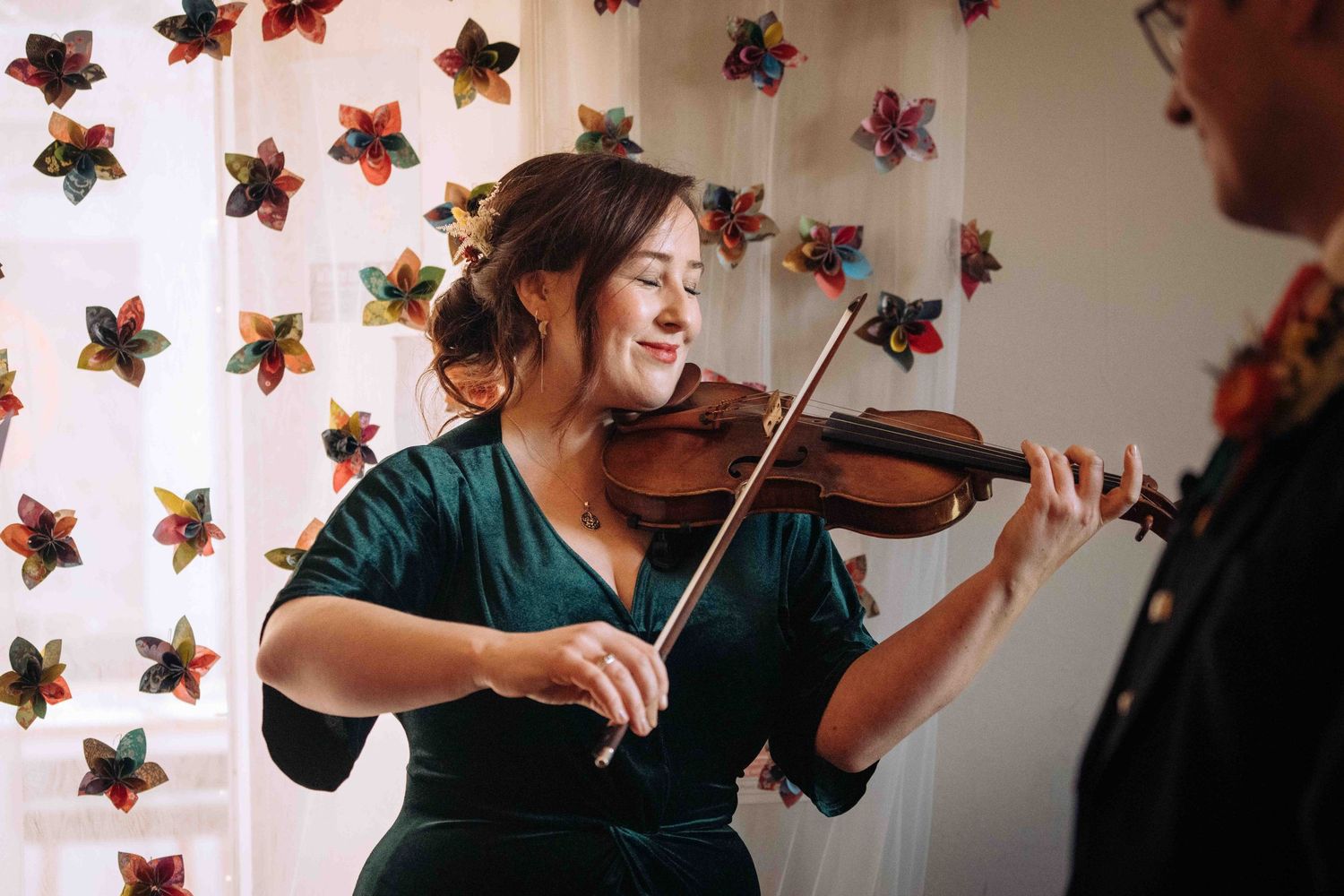 A violinist performs in a room decorated with colorful star-shaped ornaments on the wall.