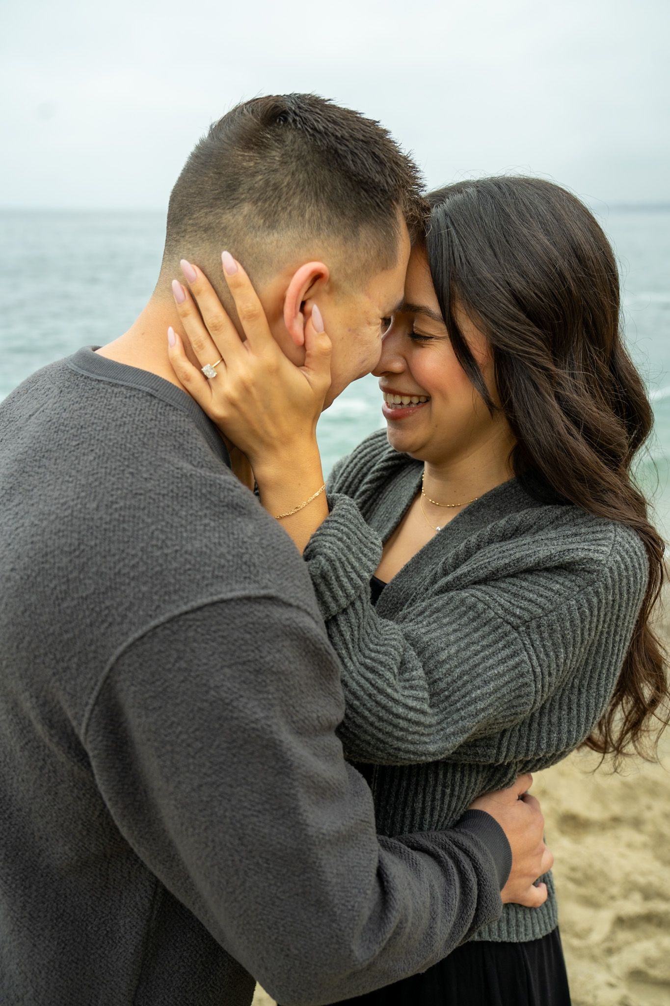 Romantic moment captured in sequence showing couple in grey sweaters by the sea.