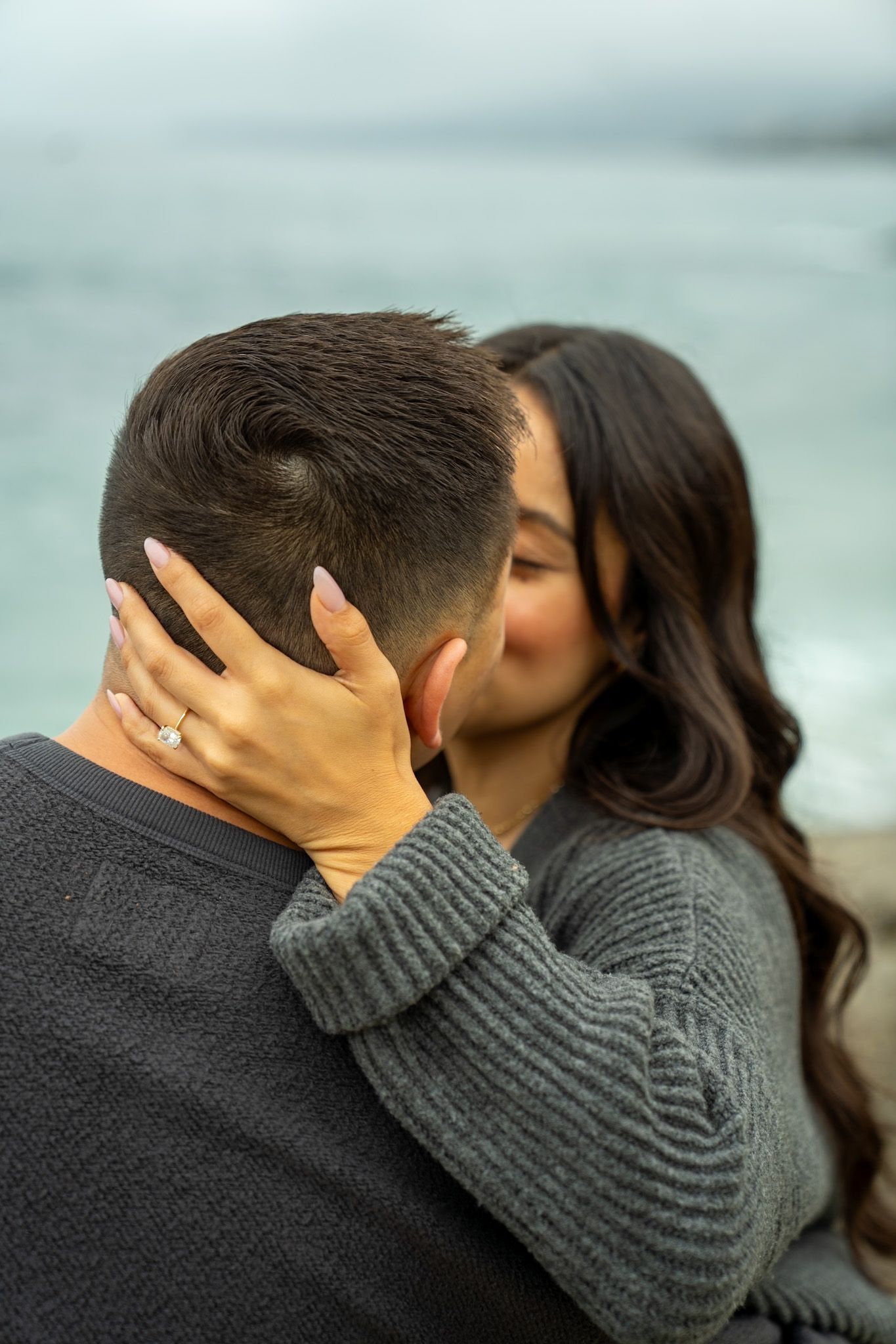 Series of intimate moments between couple wearing dark sweaters against misty ocean backdrop.