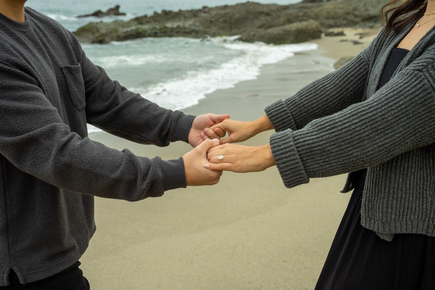 Two hands reaching out to hold each other against a rocky coastal background with crashing waves.